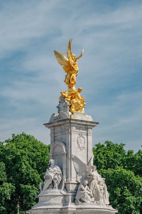 Free Dramatic view of the golden statue atop the Victoria Memorial in London, surrounded by lush greenery. Stock Photo