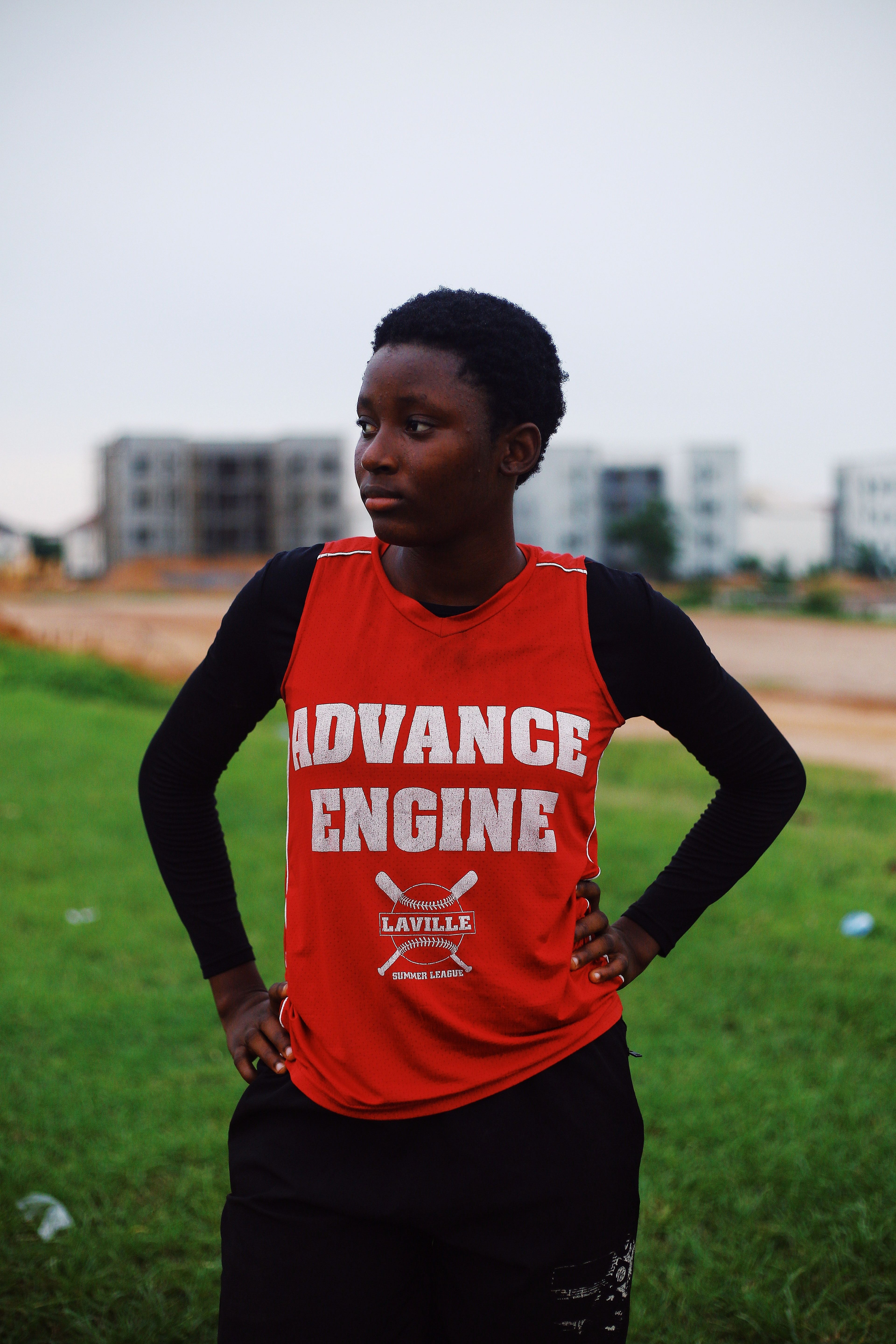 A teenager wearing a red shirt stands outdoors in Nigeria.