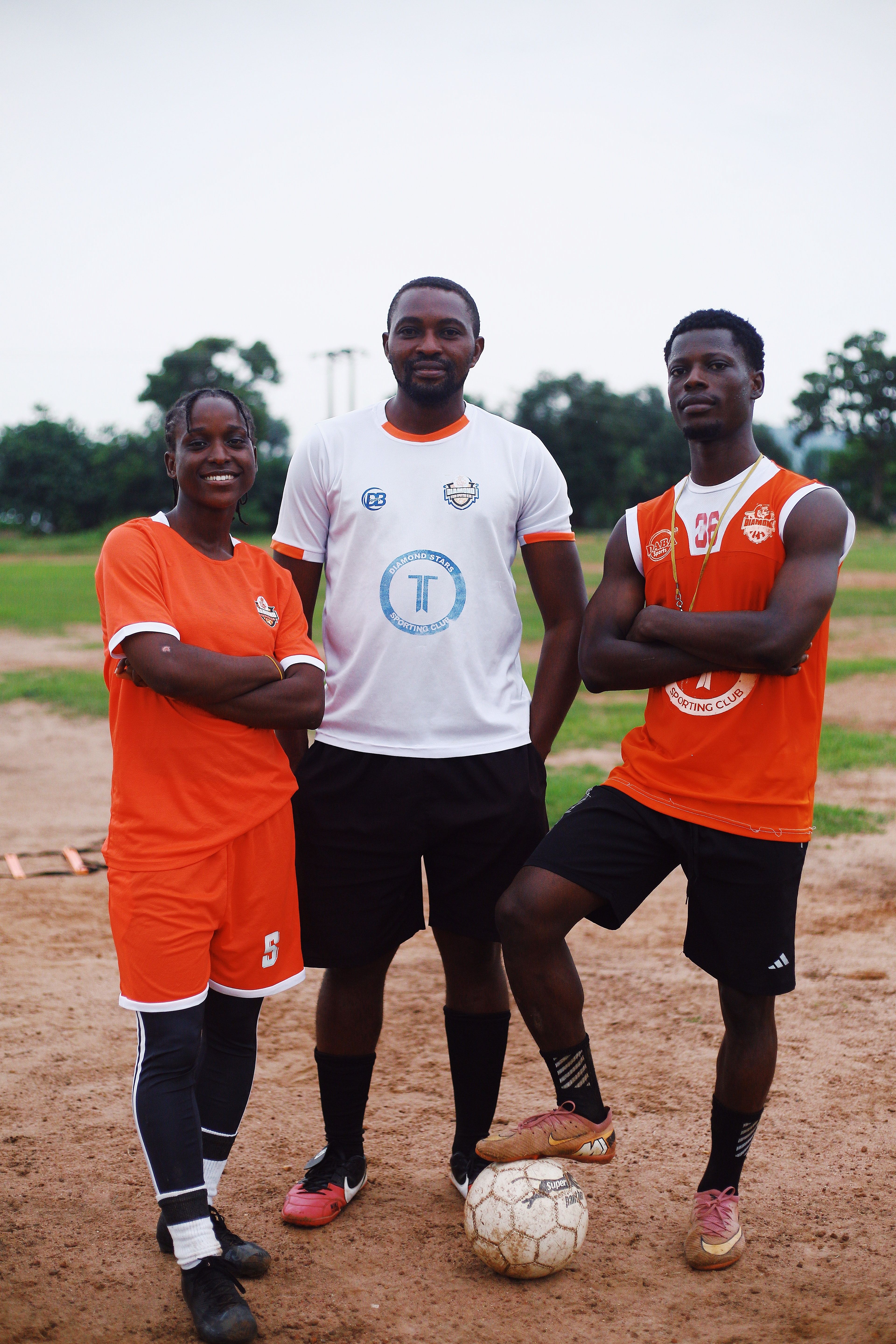 Three Nigerian football players posing on an outdoor field