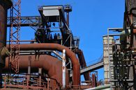 Detailed view of an industrial complex featuring rusted steel pipes and structures under a clear blue sky.