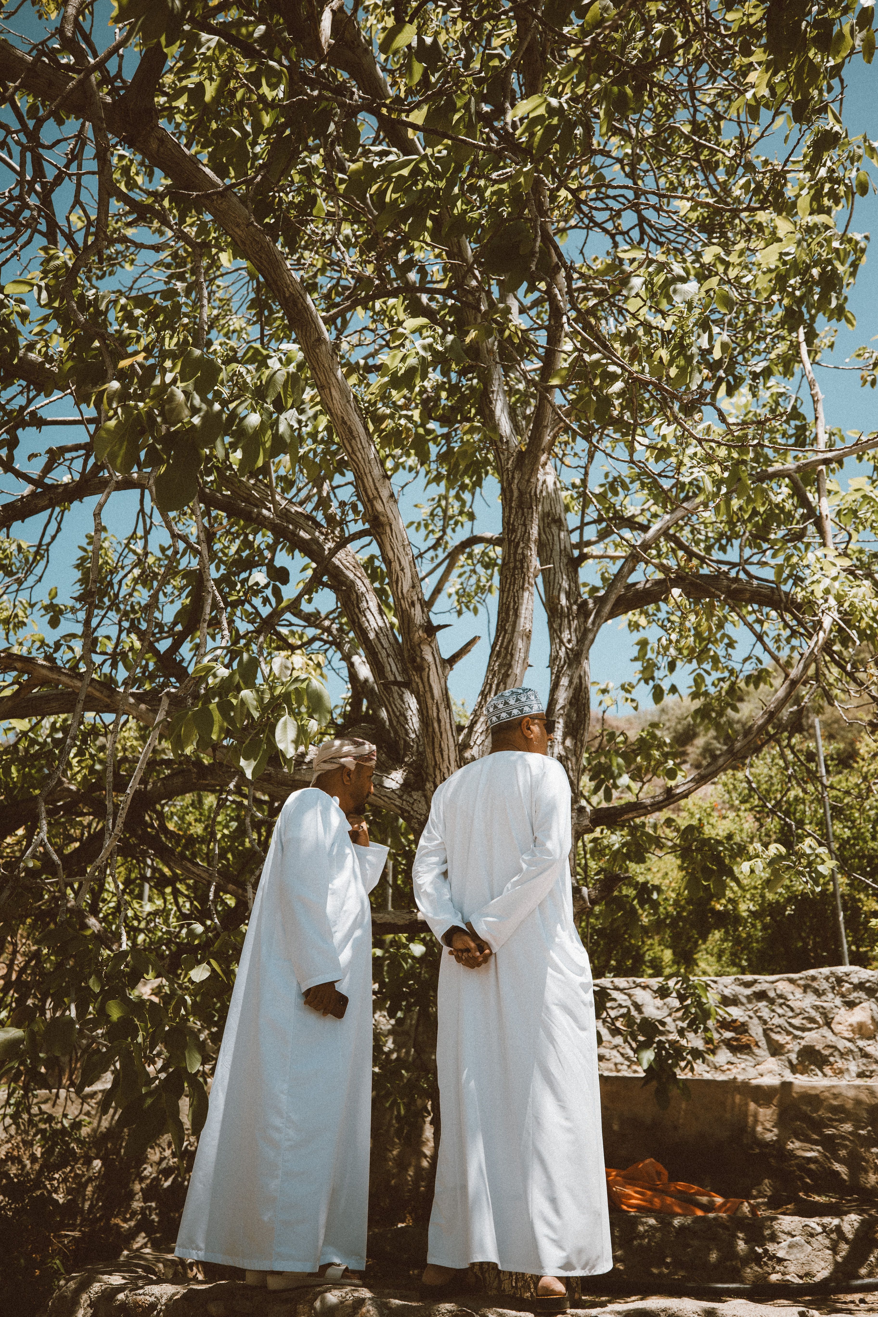 Two men in traditional Omani attire standing under a tree in Nizwa, capturing Oman's cultural essence.