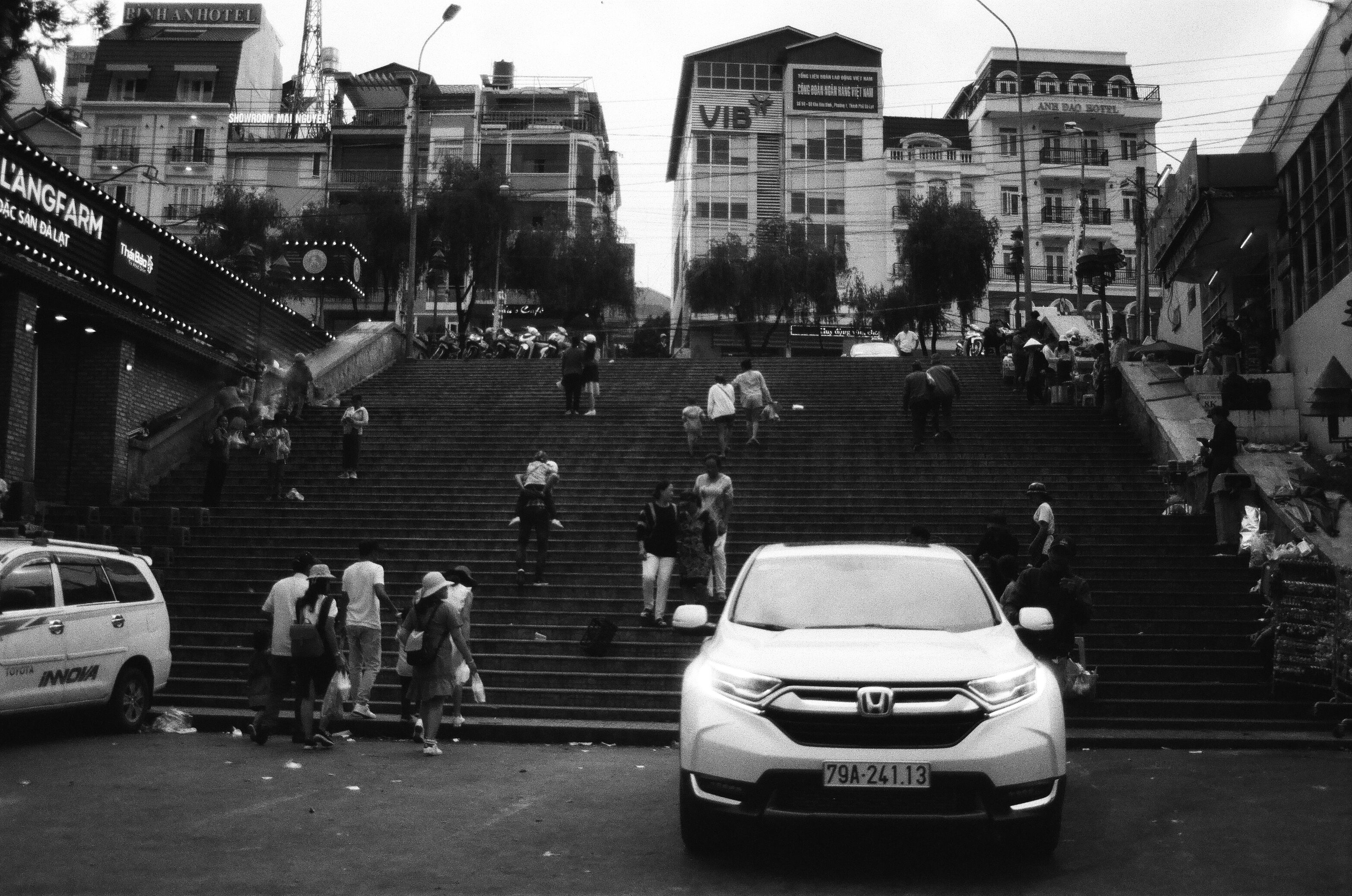 Black and white scene featuring steps and people in Đà Lạt, Vietnam, with a car in the foreground.