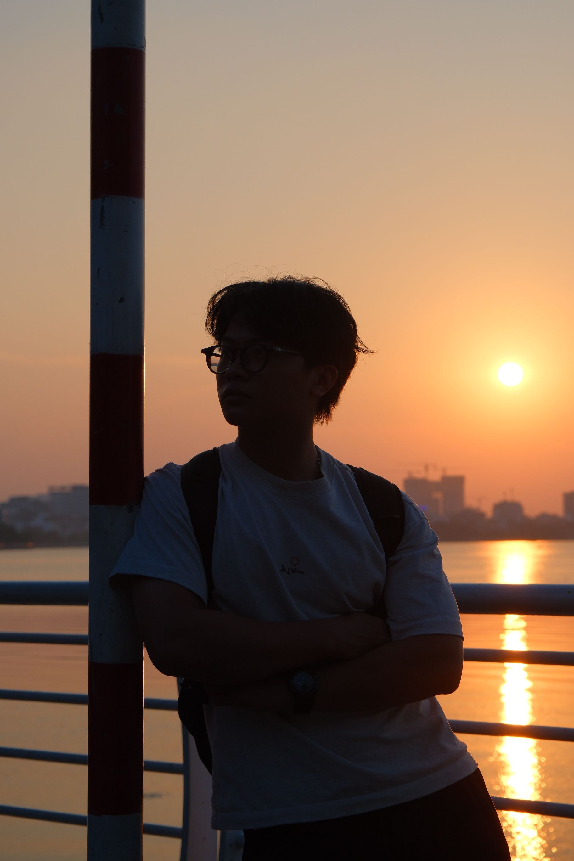 Silhouette of a person leaning on a railing by the water at sunset.