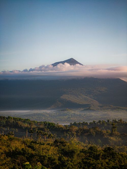 Free A breathtaking view of lush greenery with a distant volcanic mountain partially enveloped in clouds. Stock Photo