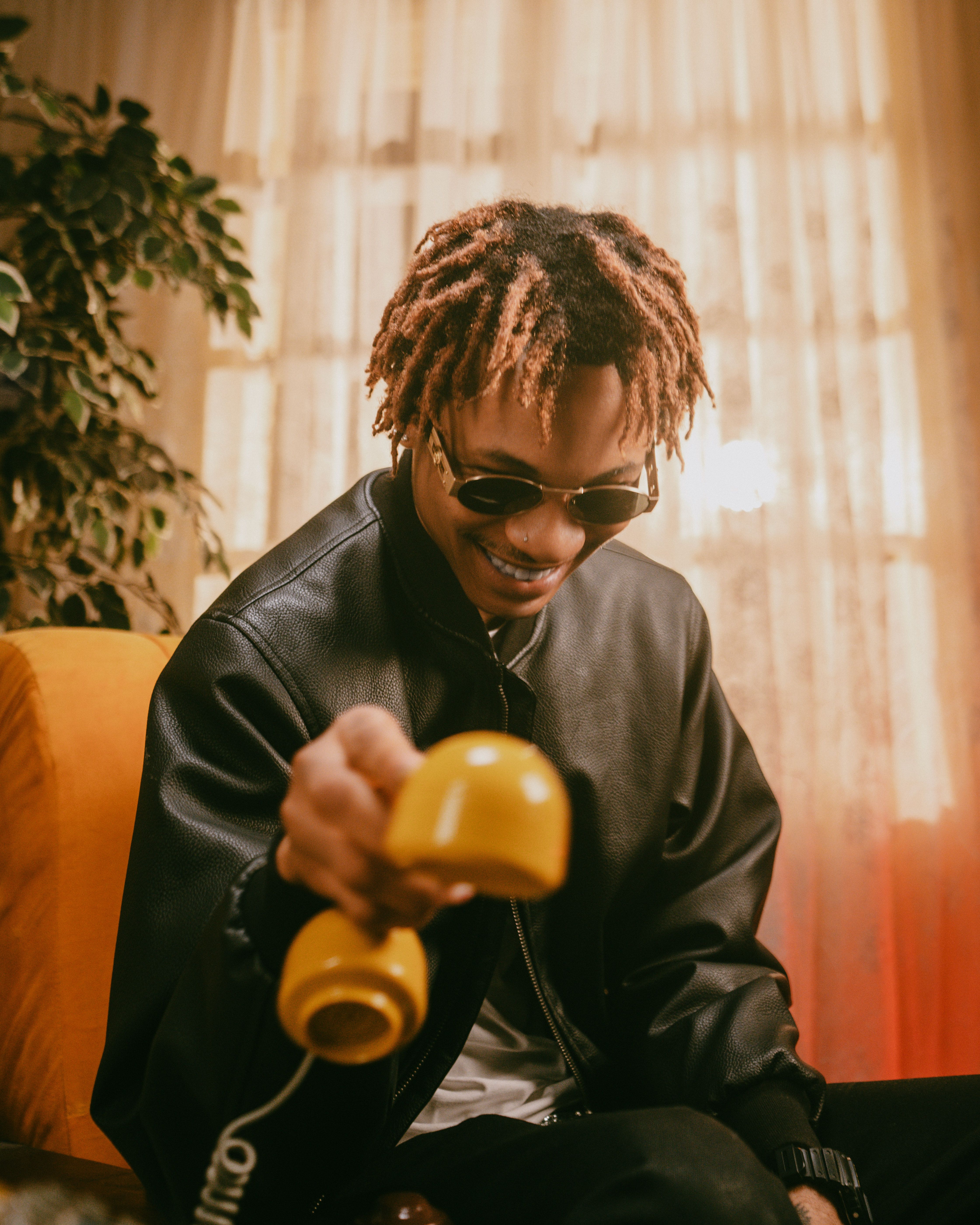 Trendy young man with sunglasses holding a yellow retro telephone indoors. Warm, relaxed vibe.