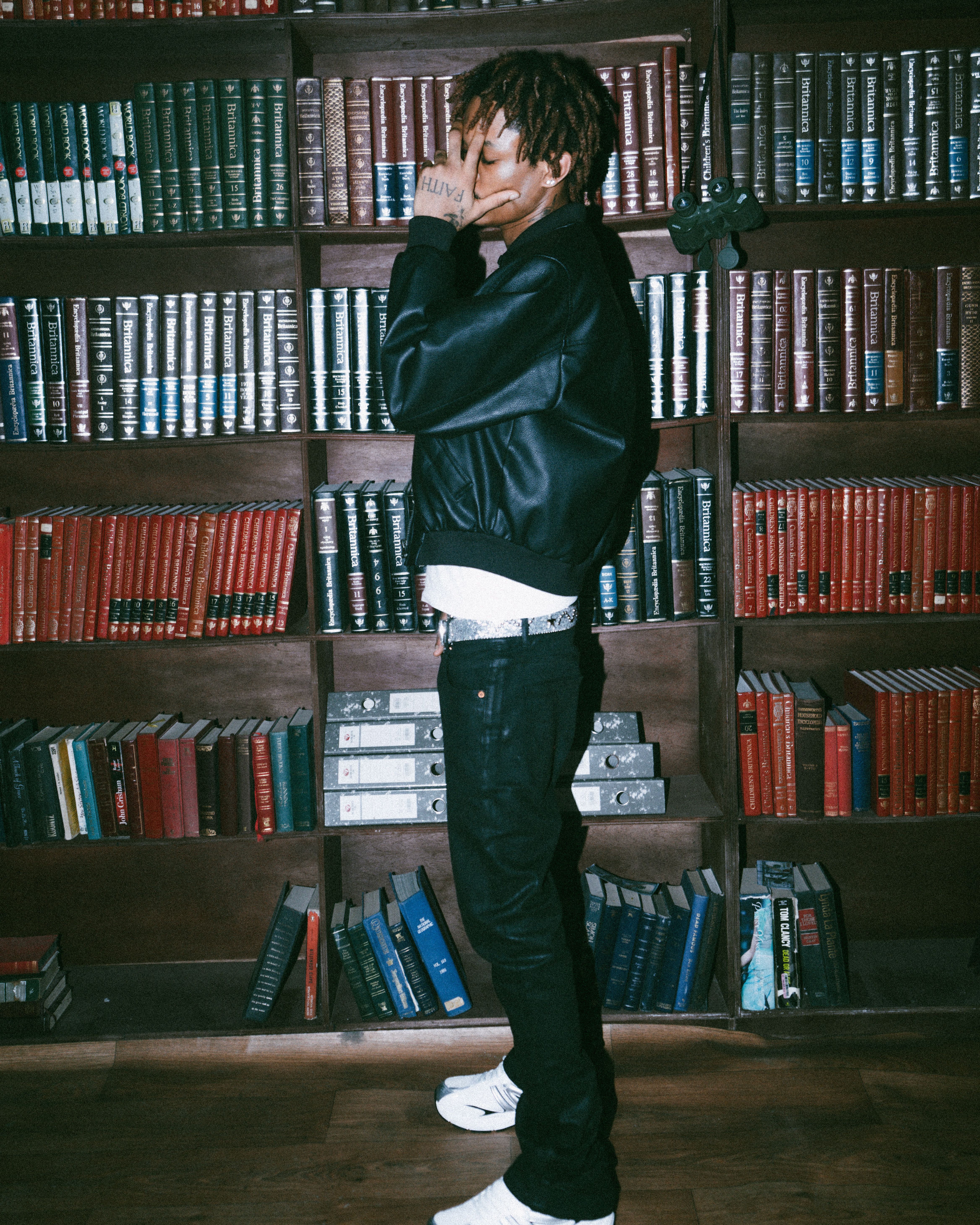 Trendy young adult with dreadlocks in a library, exuding modern style and confidence.