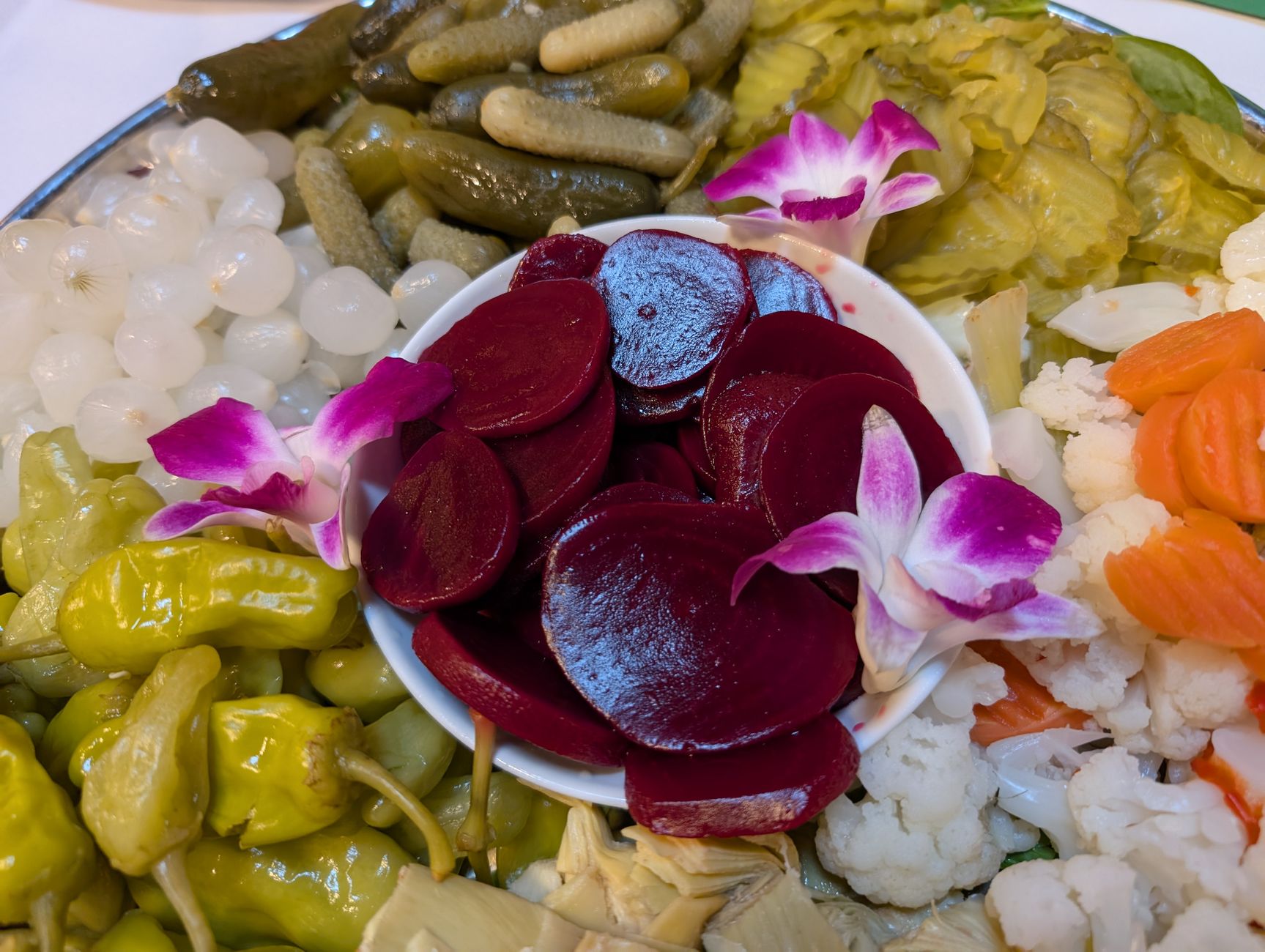 A close-up of a colorful pickle platter featuring beets, gherkins, and decorative orchids.