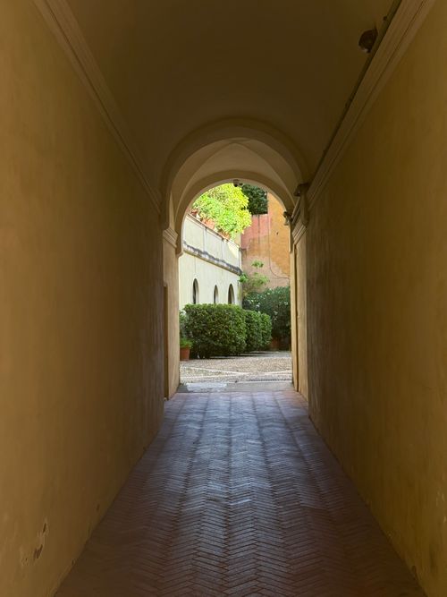 Free Quiet arched passageway in Italy leading to a sunny courtyard garden. Stock Photo