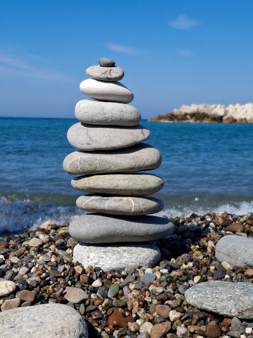 Free A serene beach scene with a stack of balanced pebbles against a blue sea backdrop. Stock Photo