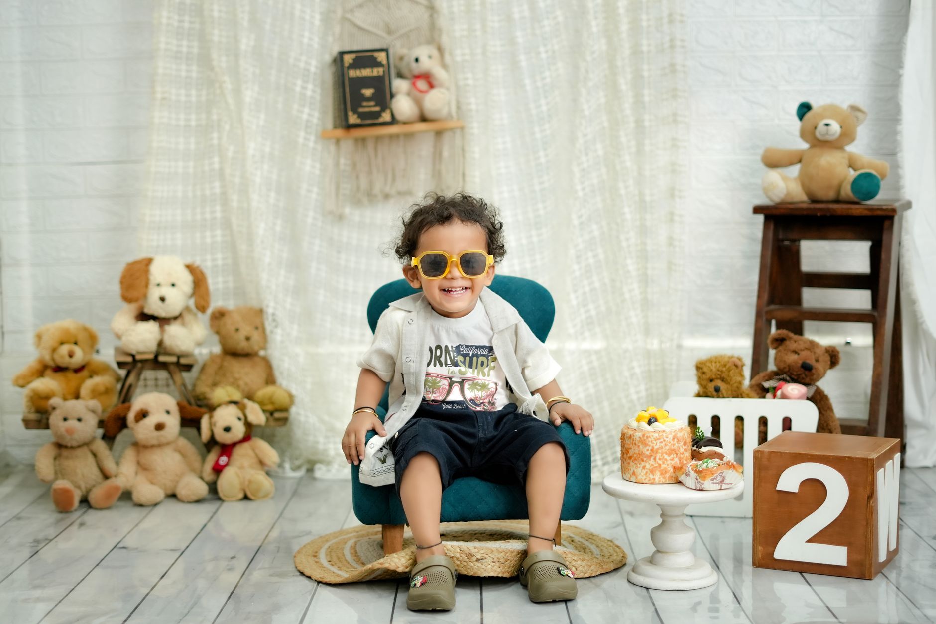 carnival themed birthday egypt — A smiling toddler with sunglasses celebrates a birthday surrounded by teddy bears and cake.