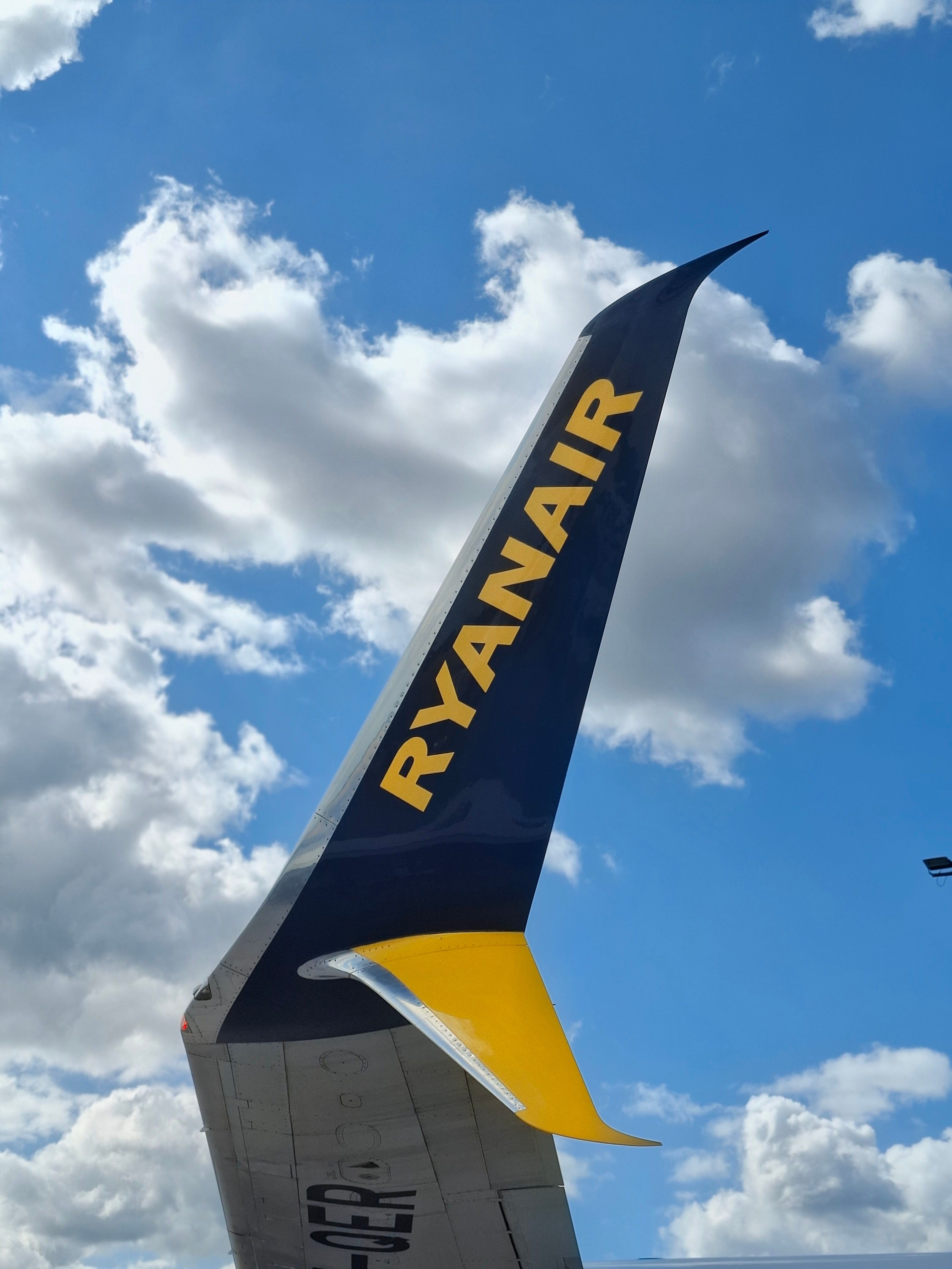 Close-up of Ryanair airplane wing tip against a vibrant blue sky with clouds.