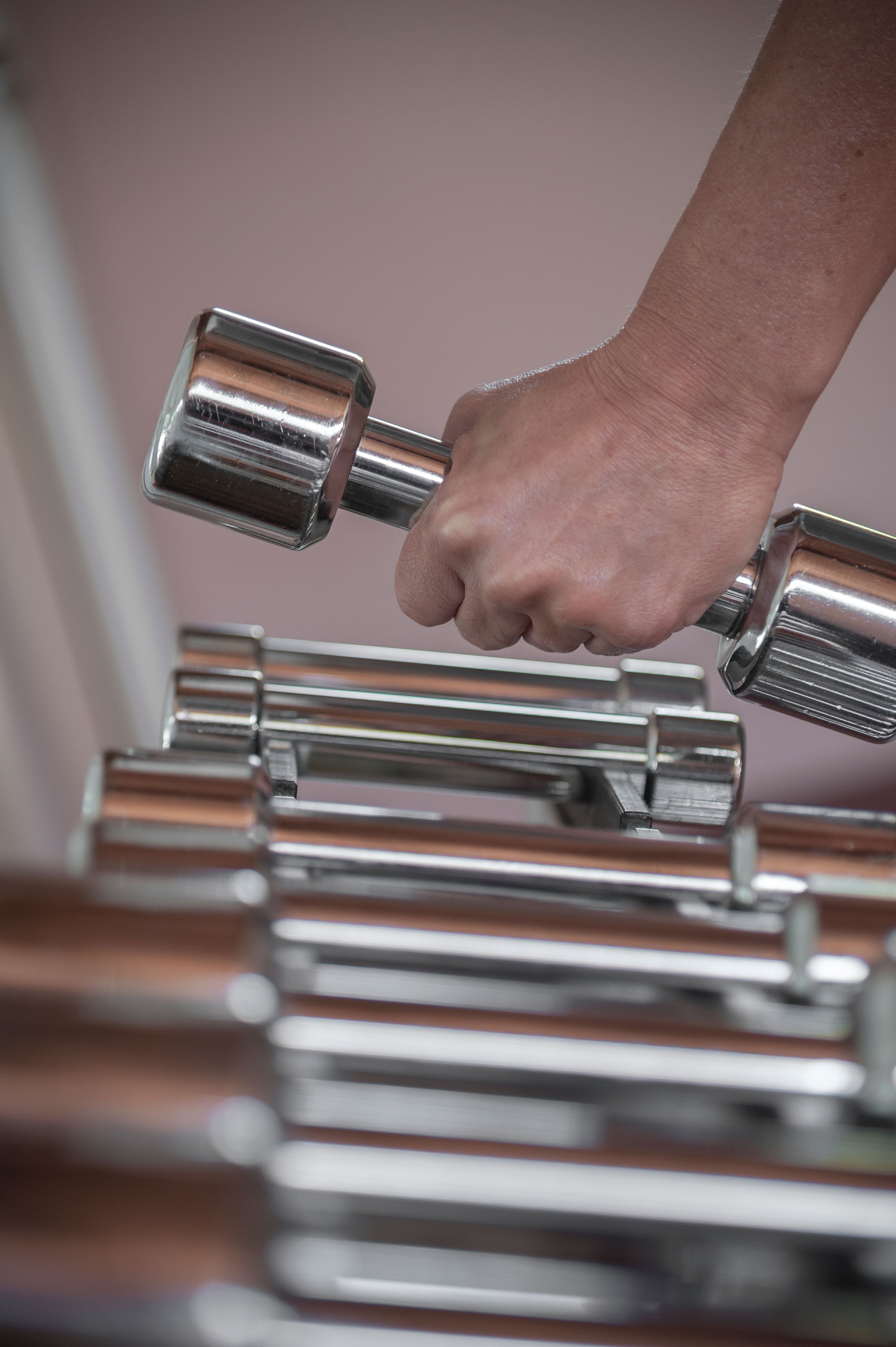 A close-up image of a person picking a dumbbell from a rack in a gym setting.