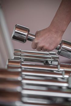 A close-up image of a person picking a dumbbell from a rack in a gym setting.