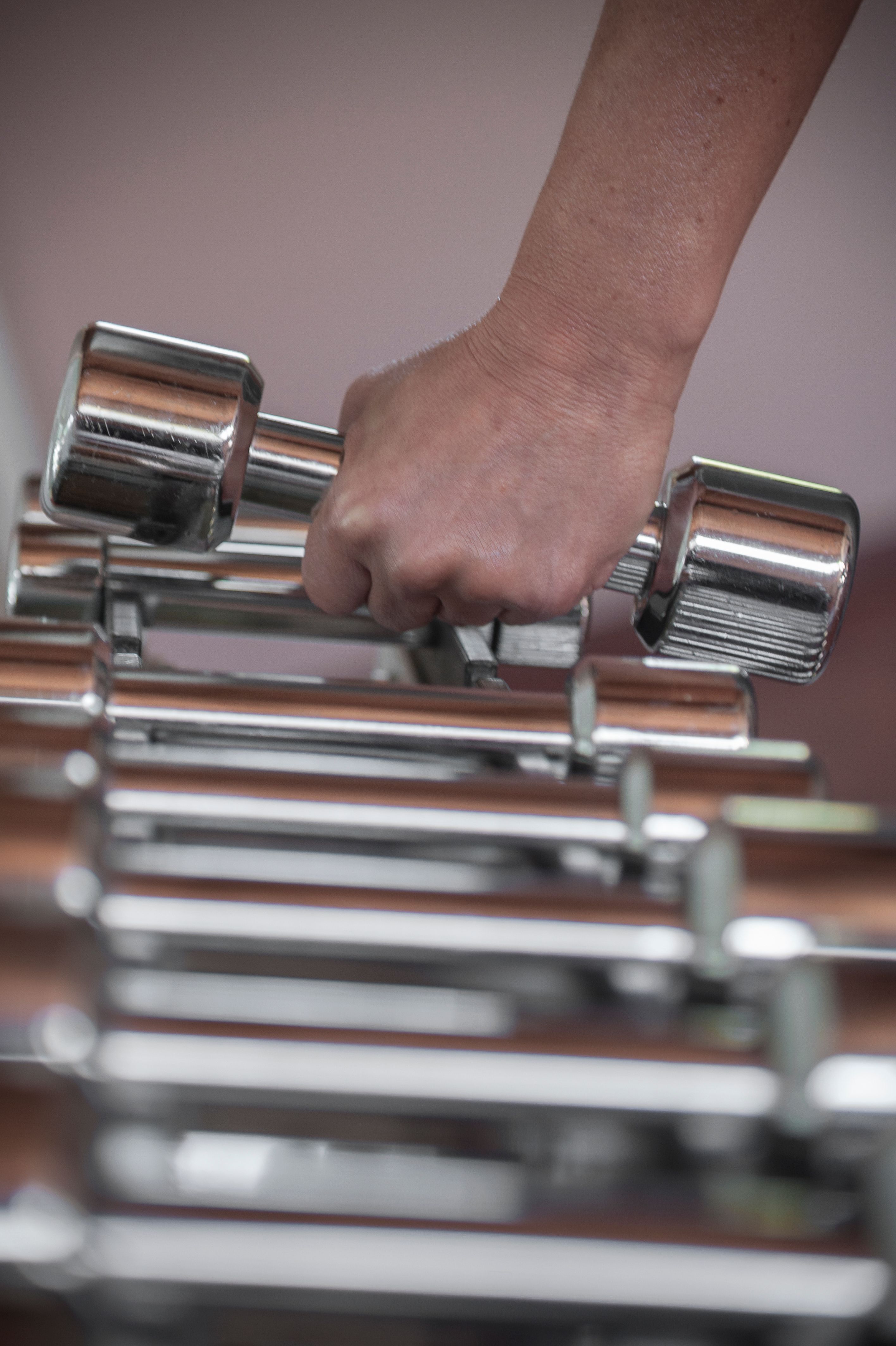 A person grabs a chrome dumbbell from a weight rack, suggesting strength and fitness.