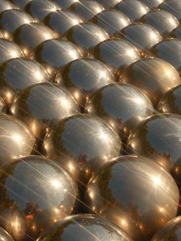 Artistic display of metallic spheres with reflections under sunlight.