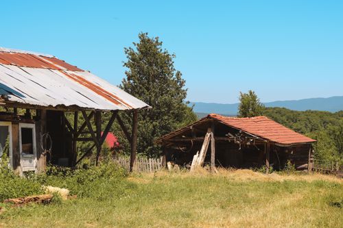 Free A scenic view of rustic farmhouses in a lush countryside under a clear blue sky. Stock Photo