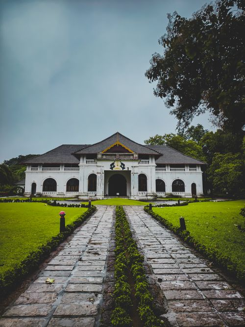 Free Elegant colonial-style building with manicured gardens and a stone path in a serene setting. Stock Photo