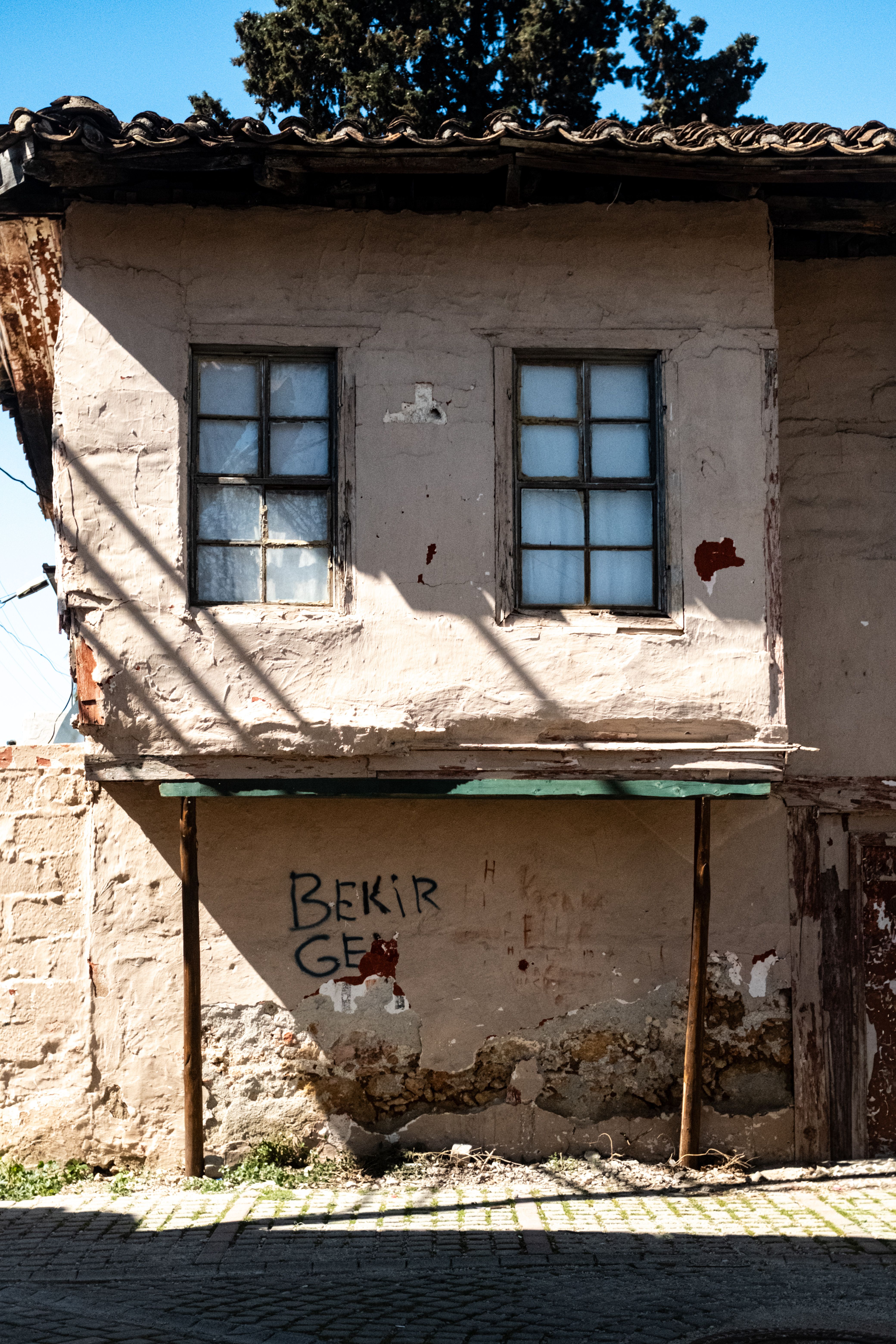 A weathered old house with peeling paint and graffiti under bright sunlight, showcasing rustic charm.