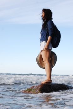 Outdoor scene of a woman standing on a rock at the beach, enjoying the summer breeze.