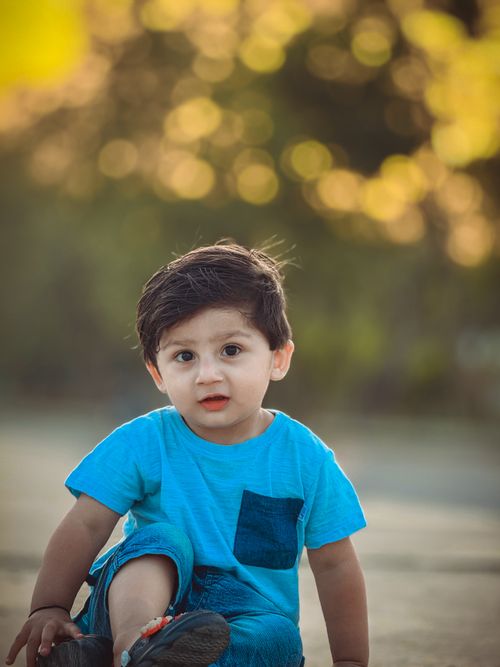 Free A young child in a blue shirt sitting outdoors in a park with a bokeh background. Stock Photo
