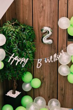 Festive indoor decor for a 2nd birthday party with green and white balloons and a 'Happy Birthday' banner.