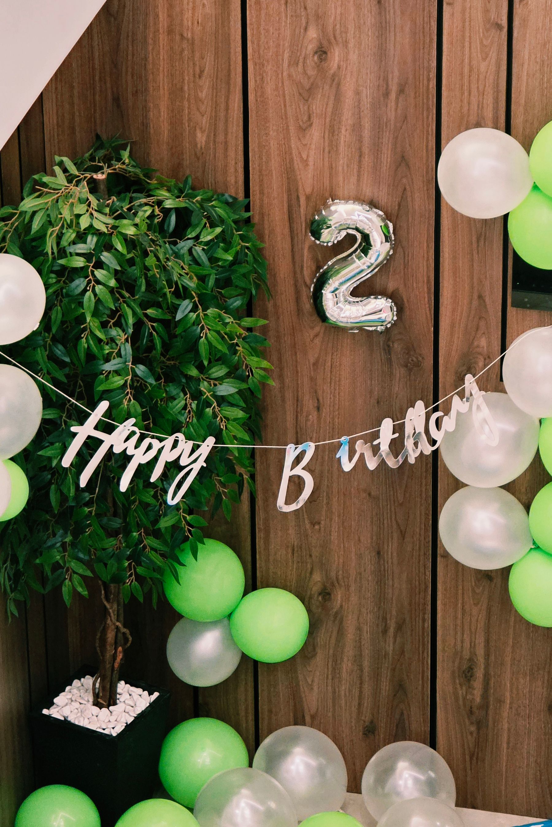 A modern green and white birthday arrangement with balloons and a celebration banner
