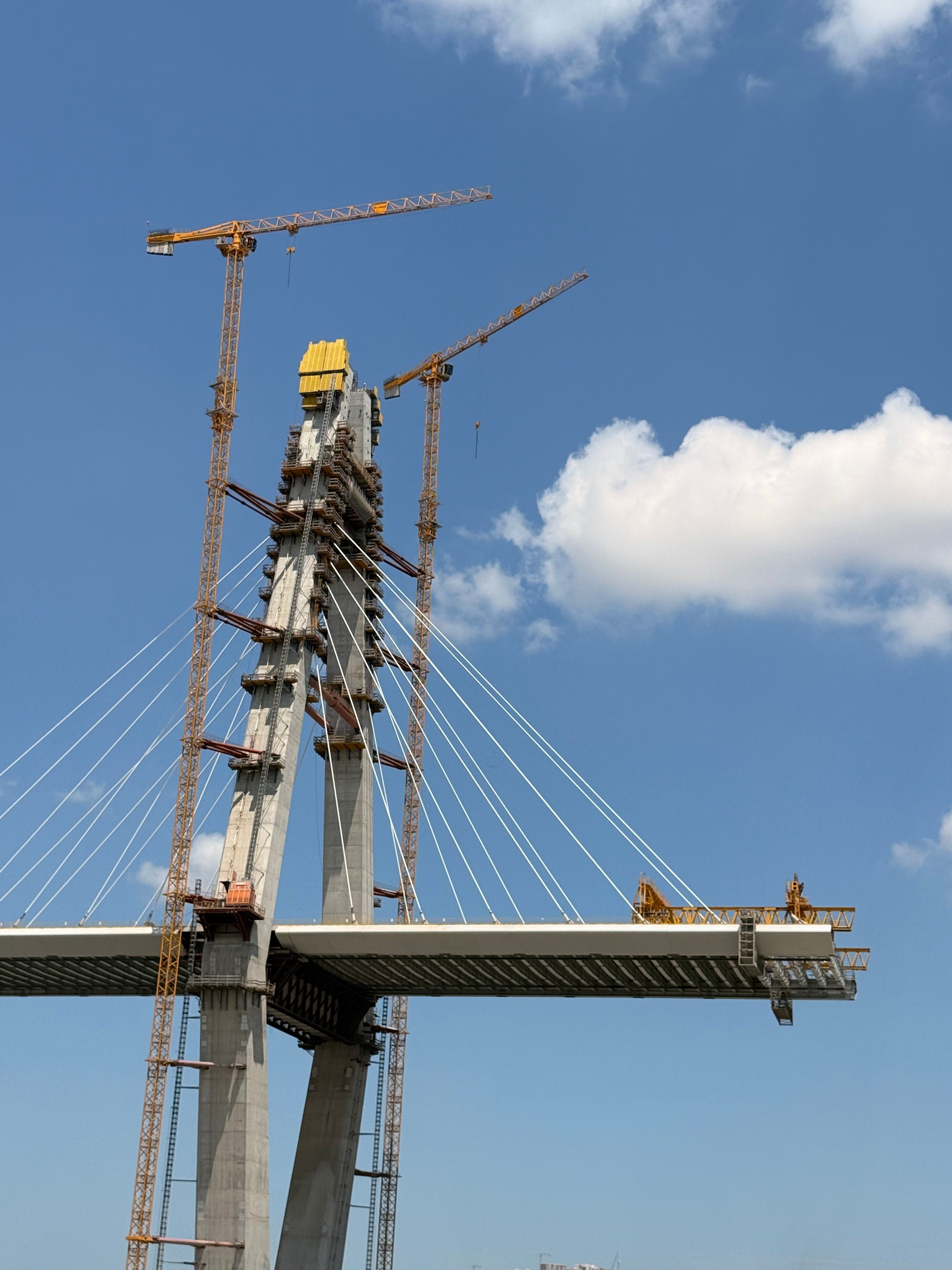 Aerial view of Yavuz Sultan Selim Bridge under construction, showcasing cranes and cables against a clear blue sky.