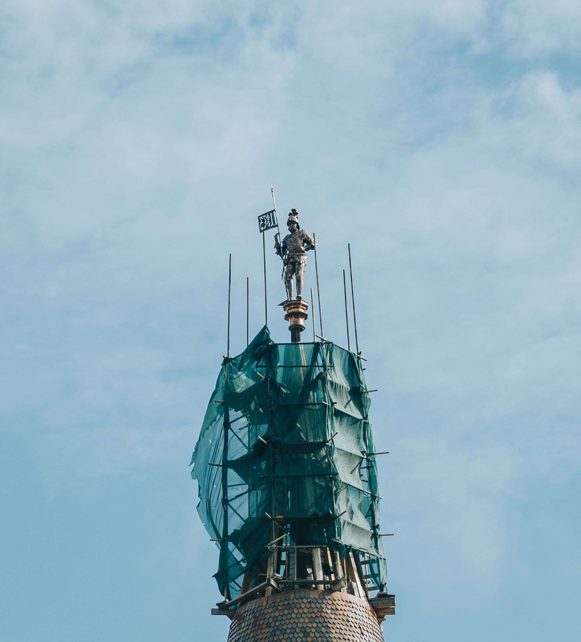 Fotomural Una estatua se encuentra en la cima de un andamiaje, cubierta con una malla de protección bajo un cielo azul claro.