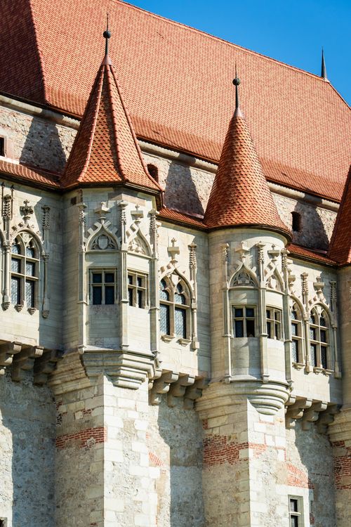 Free Close-up of a historic castle's ornate stone turrets and Gothic windows under a clear blue sky. Stock Photo
