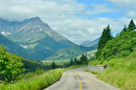 Breathtaking view of a winding road through Waterton Park, Alberta, with lush greenery and towering mountains.