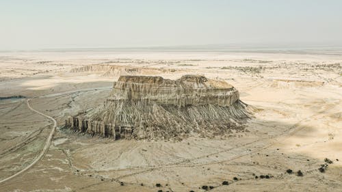 Drone view of majestic stone formation in middle of arid sandy canyon with blue sky