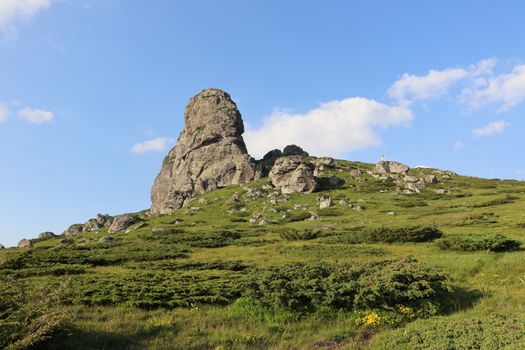 A stunning rocky hill under clear skies, surrounded by lush greenery.
