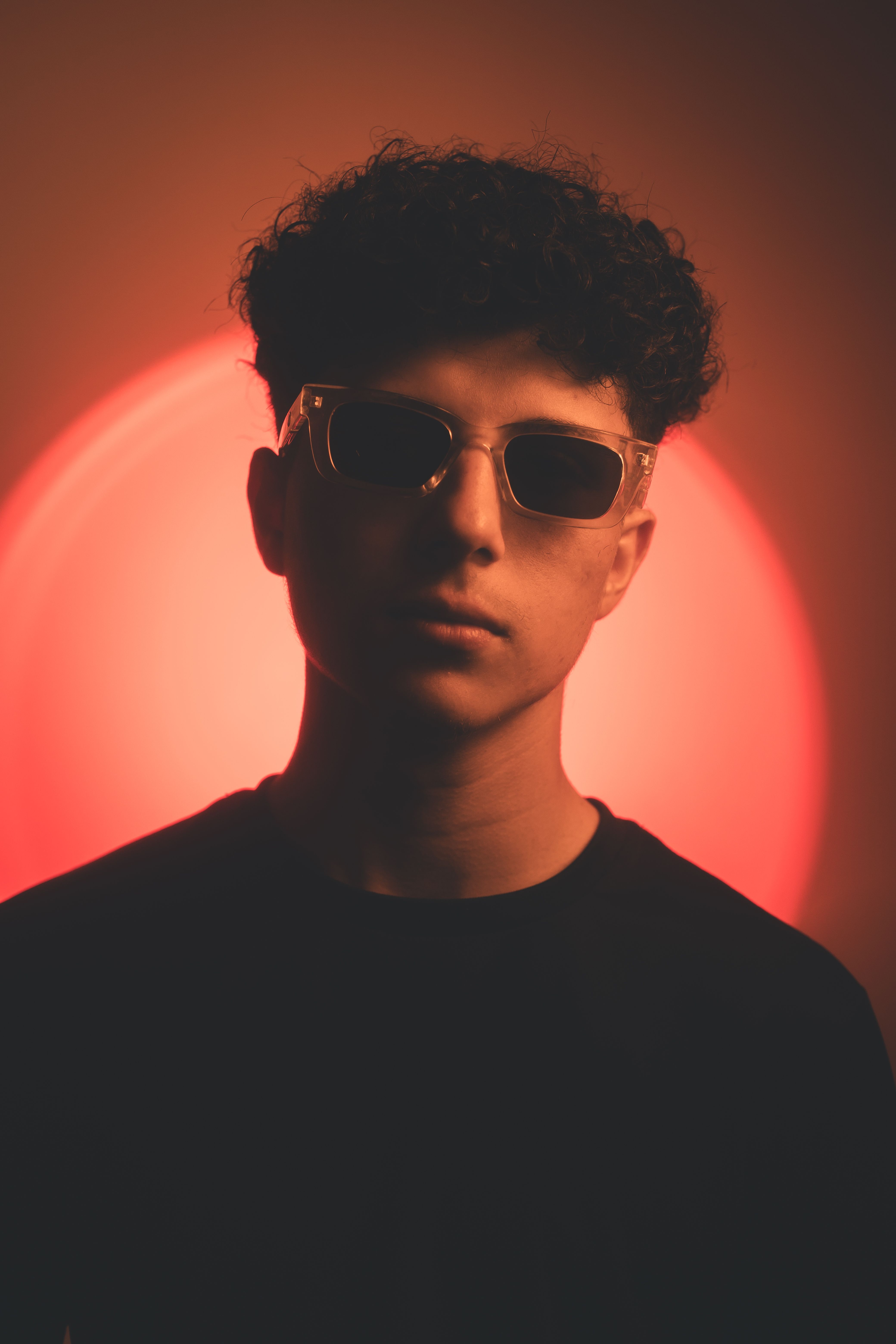 Artistic portrait of a young man in sunglasses against a red-lit background, conveying a mysterious vibe.