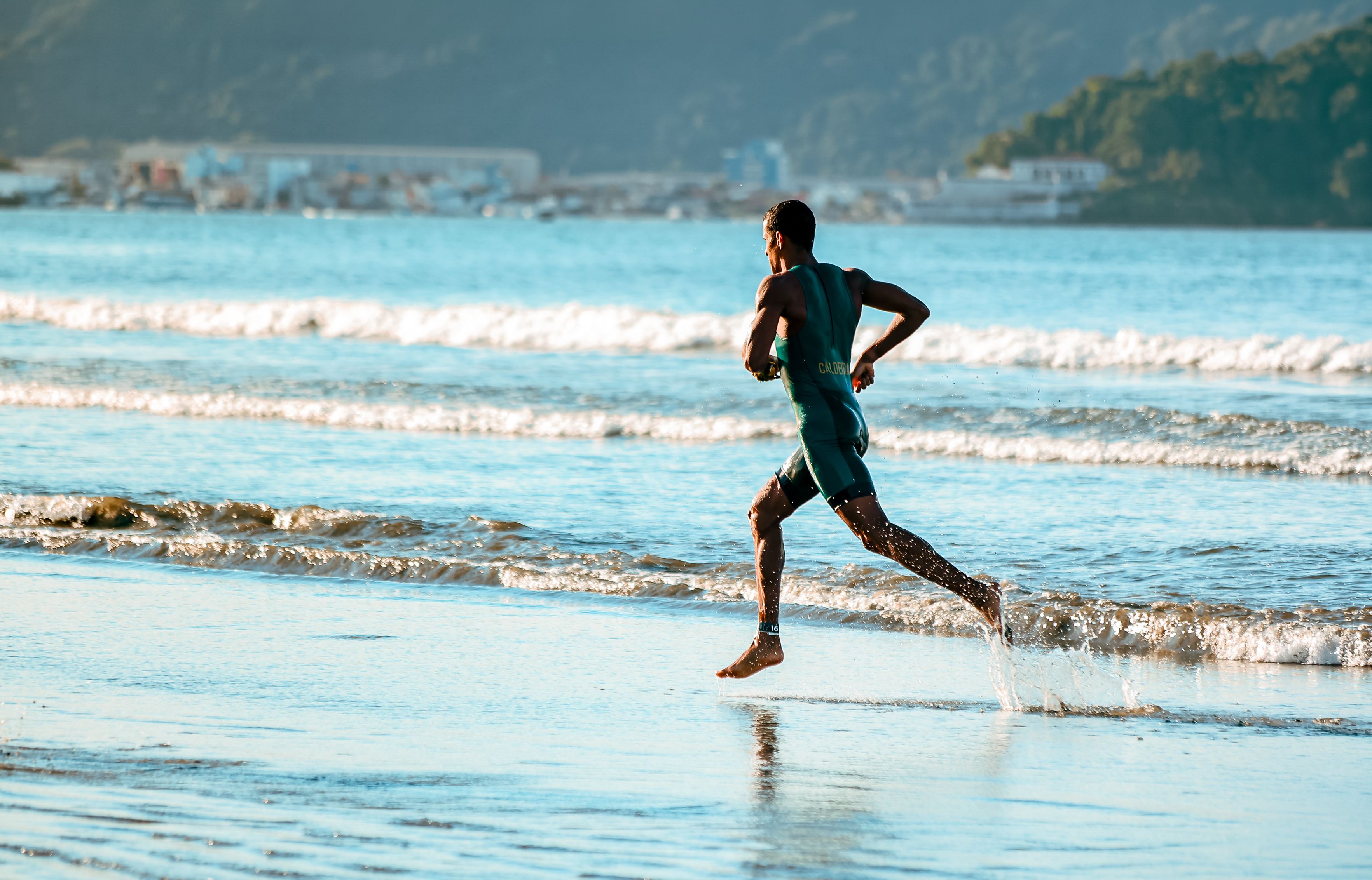 Lone runner sprinting along the shoreline at golden sunrise, warm low light and long shadows on wet sand