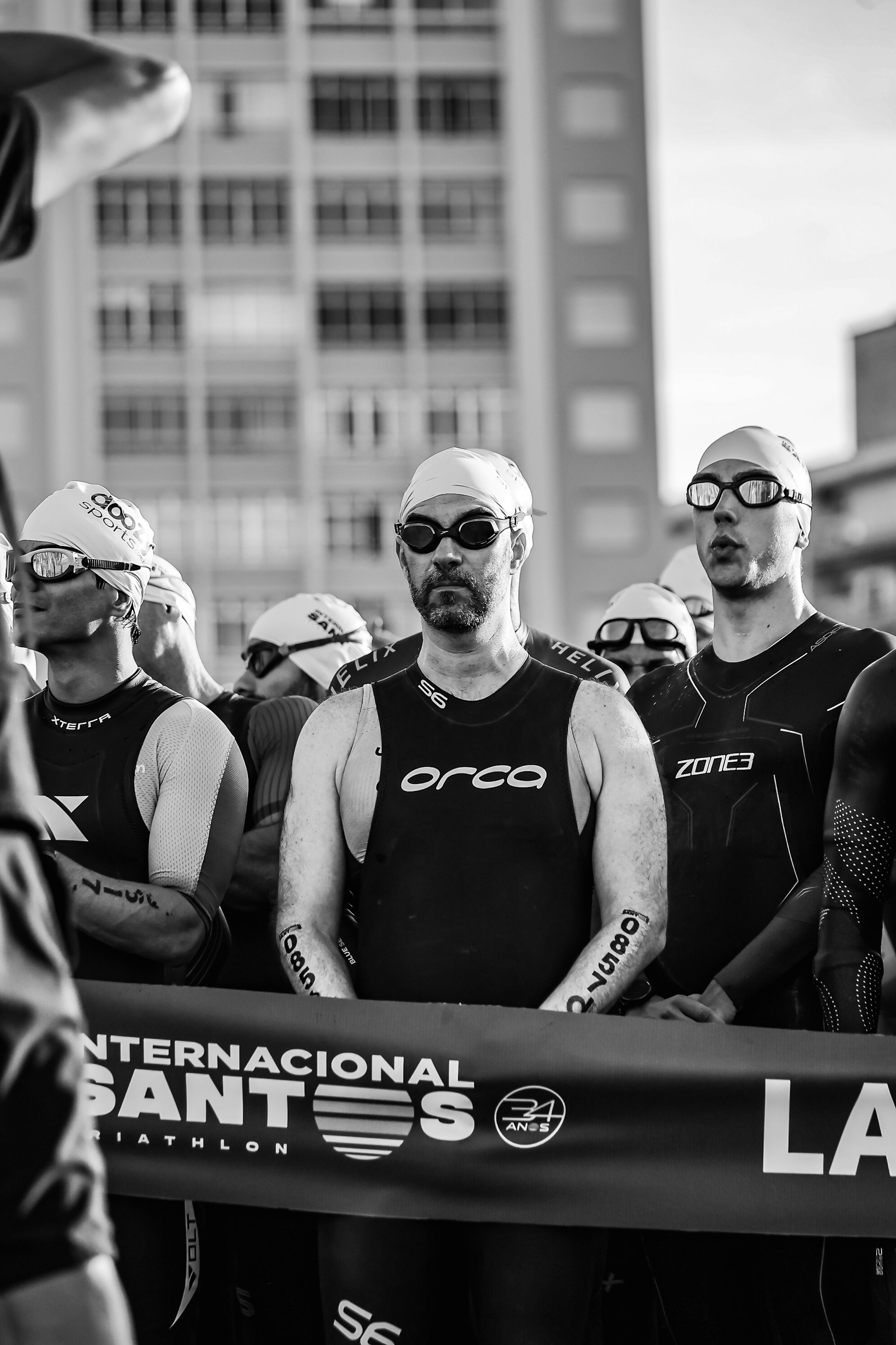 Athletes wearing wetsuits and goggles at starting line of Santos Triathlon.