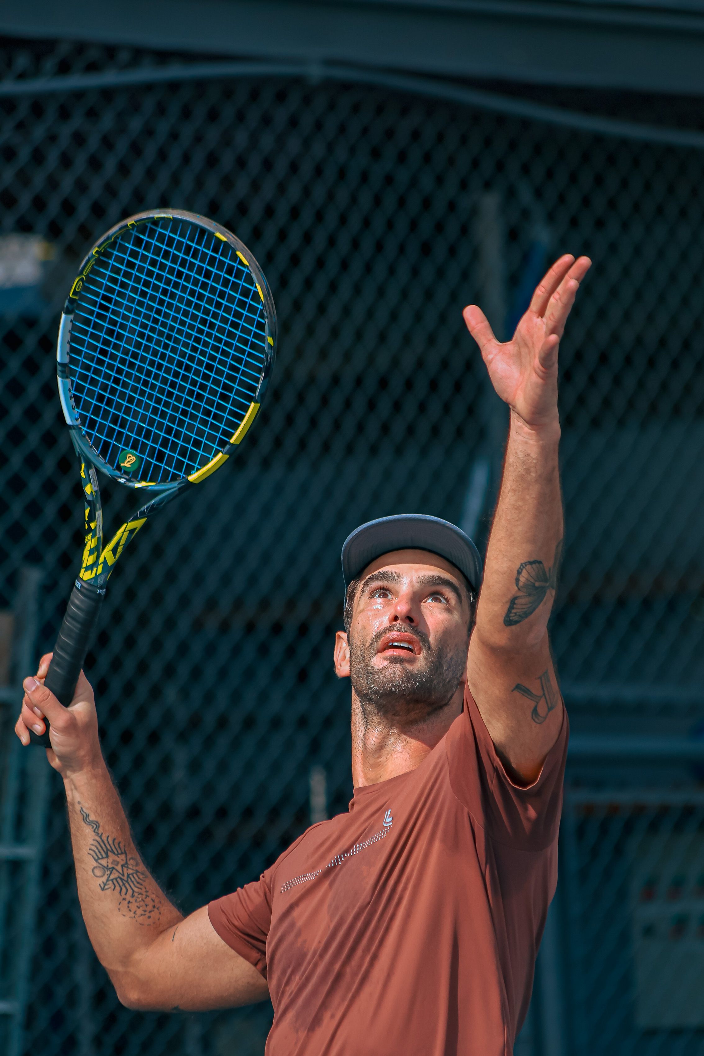 Focused male tennis player preparing to serve on an outdoor court under daylight conditions.