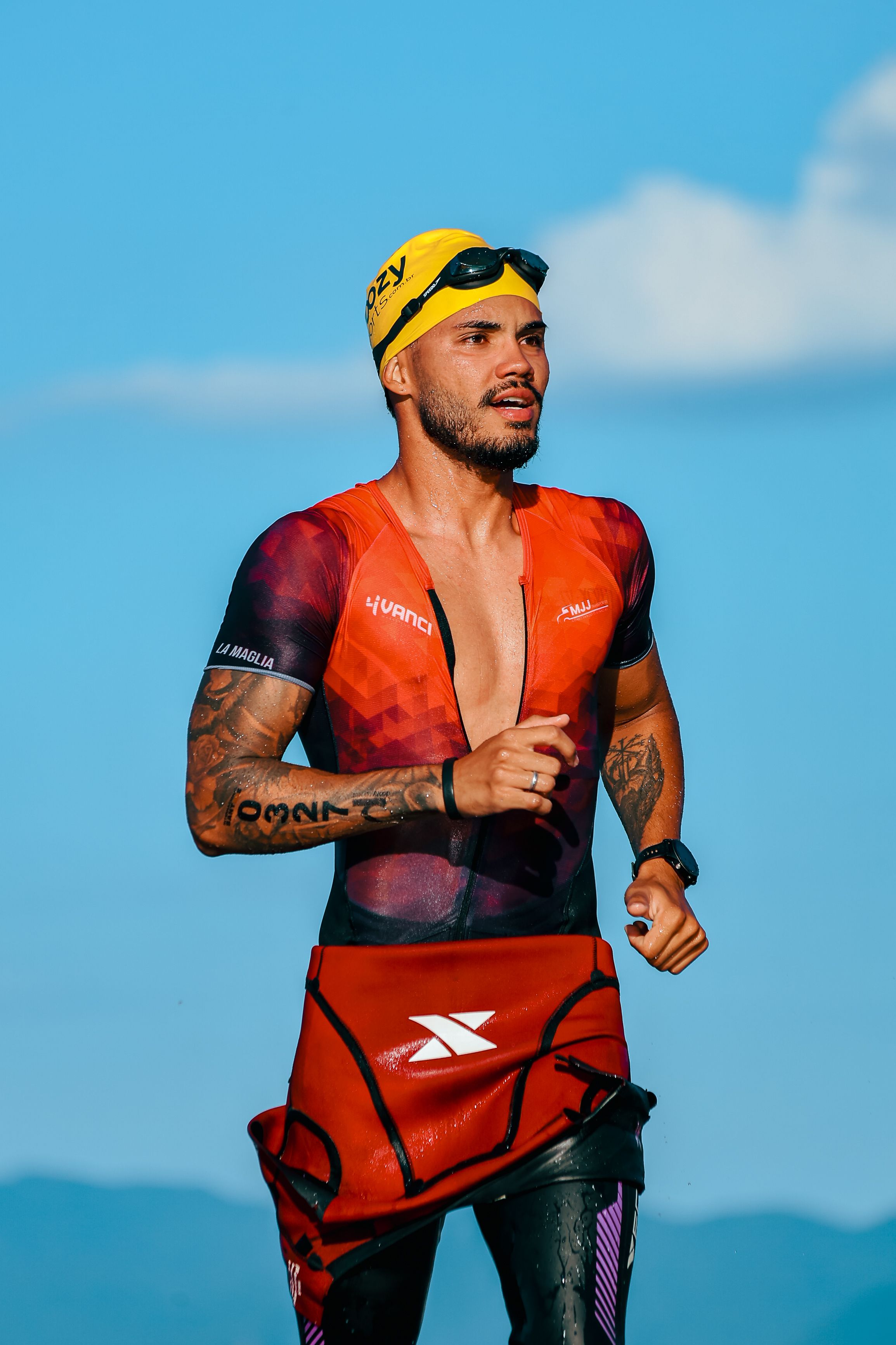 Focused male athlete running in a triathlon, wearing colorful gear against a clear sky.