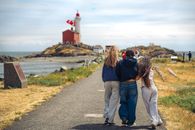 Three friends walk towards a lighthouse on a sunny day in Victoria, British Columbia, Canada.