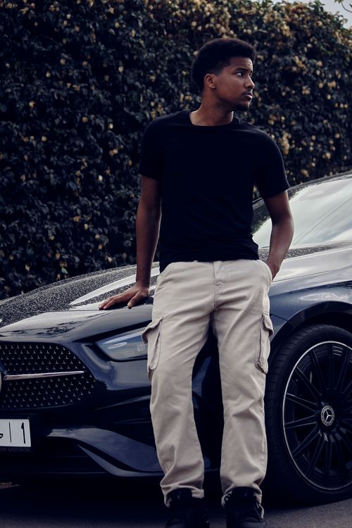 Free Stylish young man in urban setting leaning on a luxury black sedan. Stock Photo