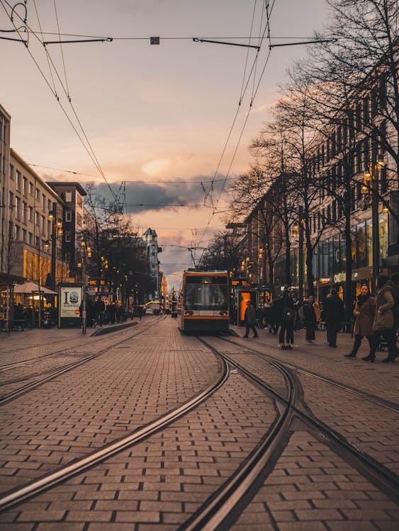 Modern tram on railroad with people walking in old town with low rise buildings in cold twilight