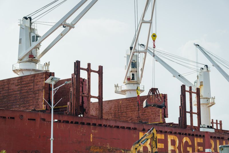 Cargo ship docked at an industrial port with cranes unloading cargo under clear skies
