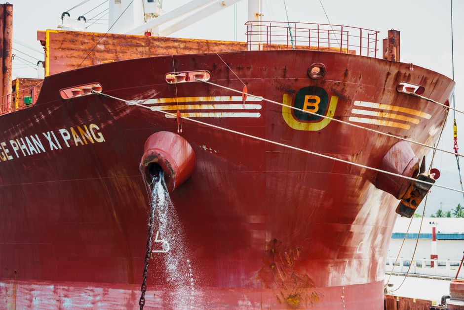 Front view of a red cargo ship docked at a port, releasing water.