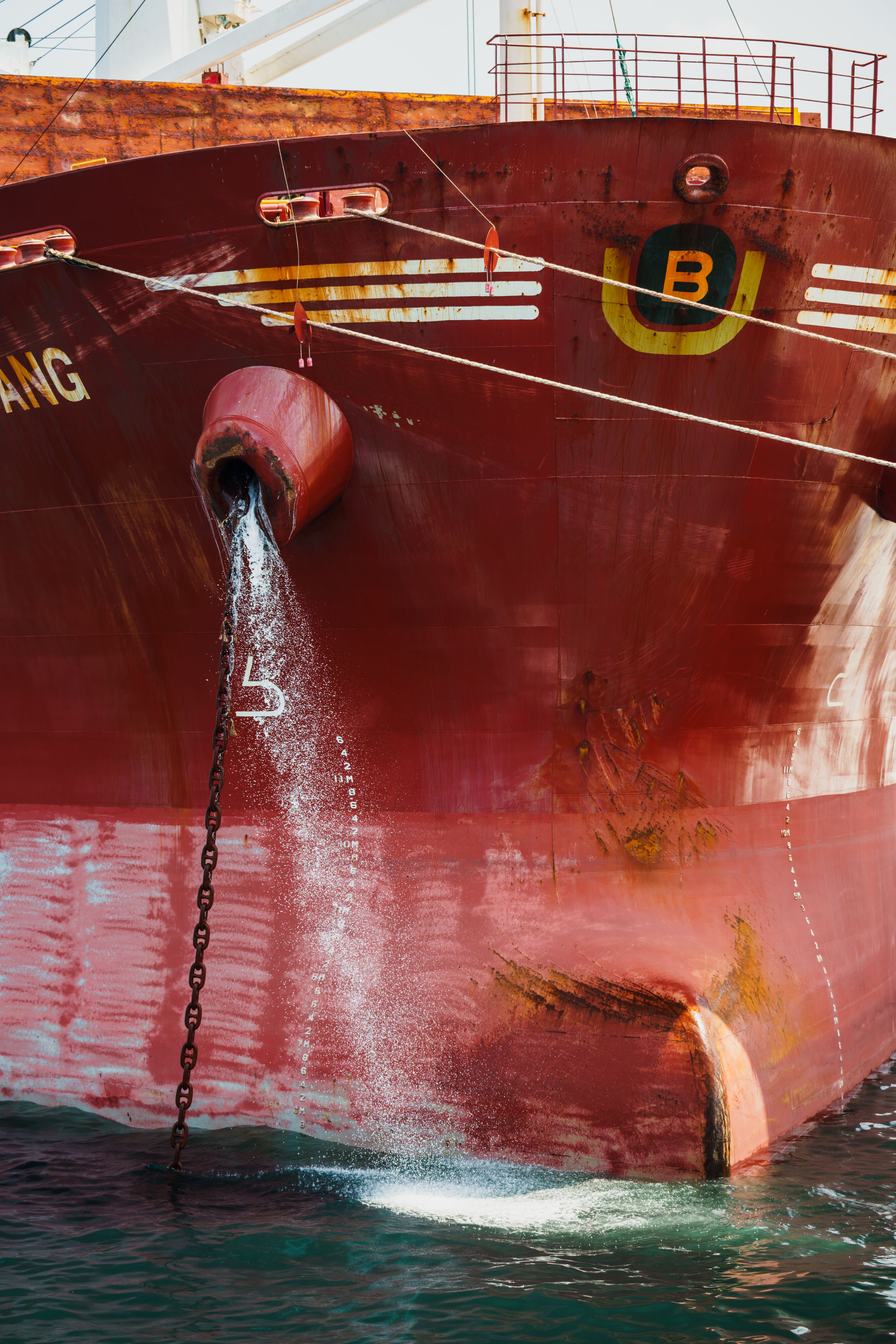 Detailed view of the bow of a red cargo ship with anchor chain and flowing water.