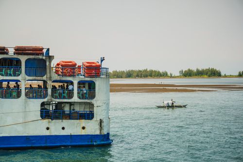 Free Ferry and small fishing boat navigating a peaceful sea with a distant treeline. Stock Photo