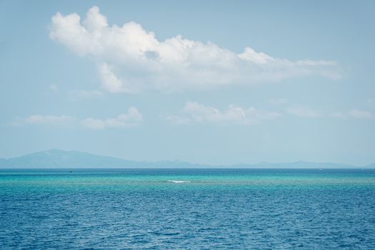 Calm and serene ocean landscape with a cloudy blue sky and distant mountains.