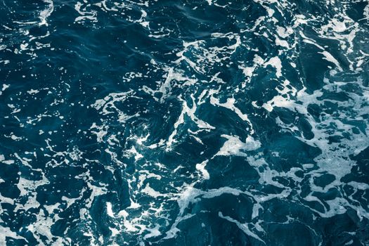 A mesmerizing view of the deep blue ocean with intricate white foam patterns captured from above.