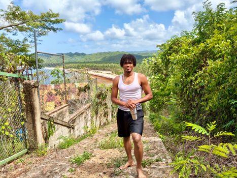 Man walking on a picturesque coastal path surrounded by lush greenery and ocean views on a sunny day.