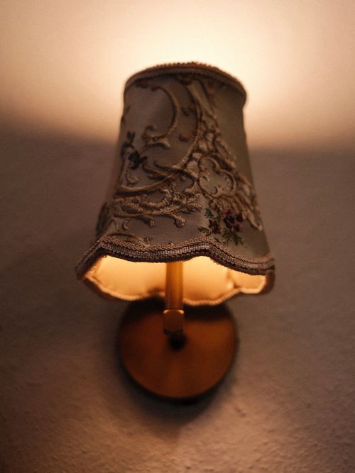 Free Elegant vintage wall sconce featuring an intricate embroidered lampshade, casting a warm glow. Stock Photo