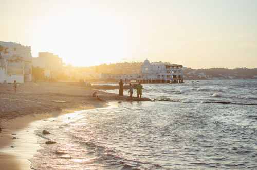 Free Serene beach setting at sunset with distant people, waves, and buildings. Stock Photo
