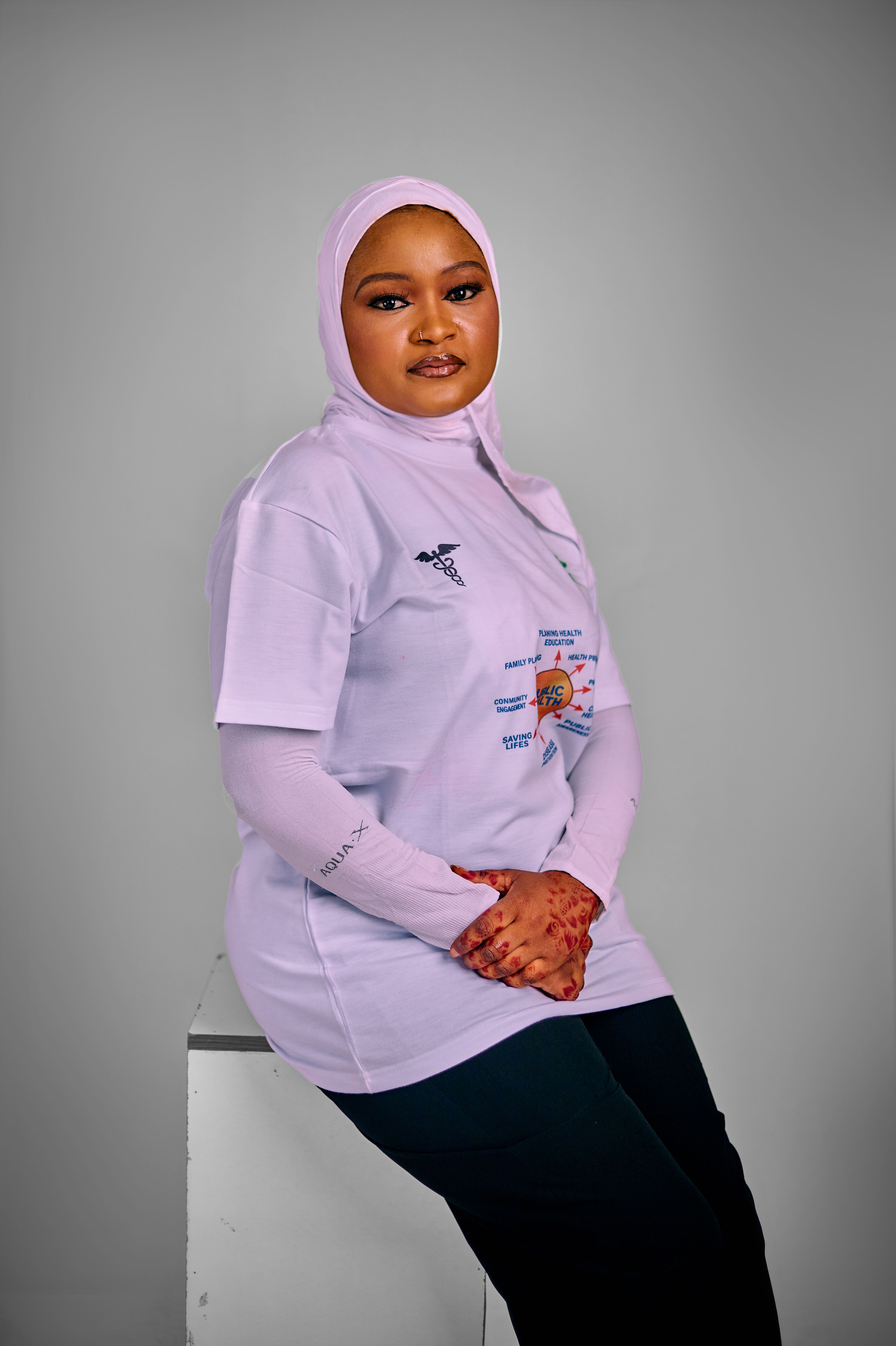 Portrait of a confident woman in casual attire and hijab, set against a neutral grey backdrop.
